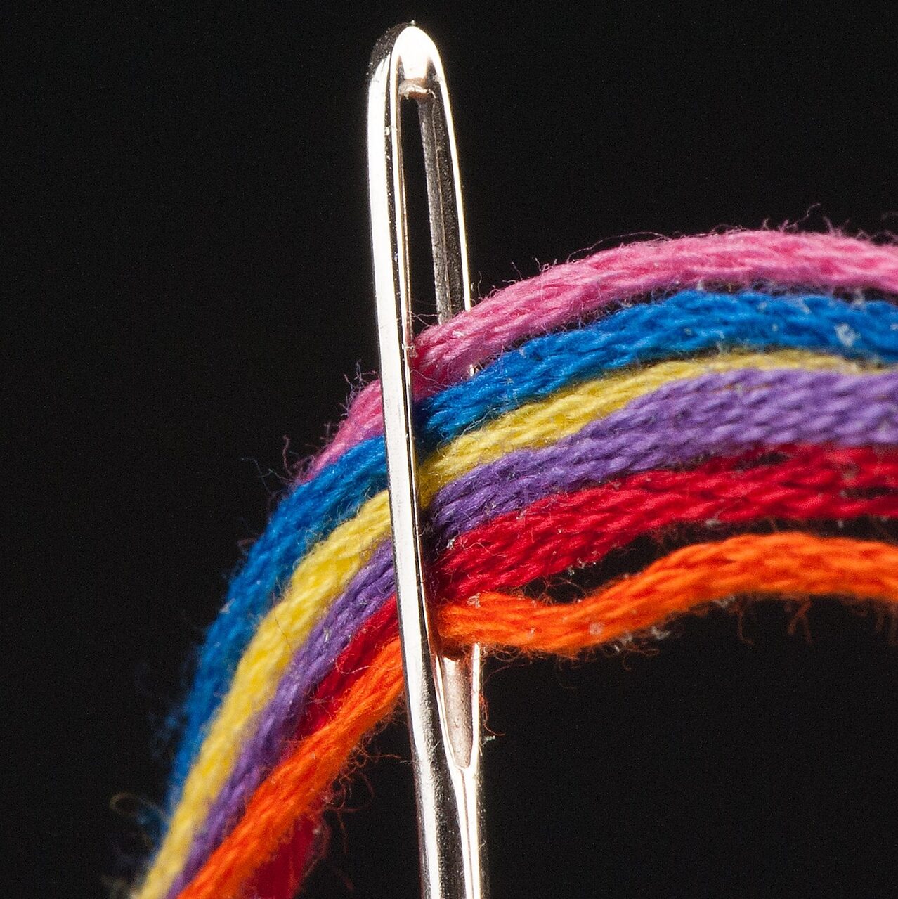 Fils rose , bleu , jaune , violet , rouge et orange qui passent dans une aiguille