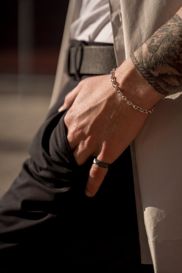 Close-up of a man's hand showcasing fashion accessories like a bracelet, ring, and tattoo under stylish lighting.